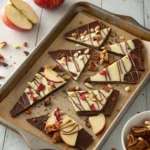 Pieces of candy apple bark with chocolate, apple slices, and nuts on a rustic tray