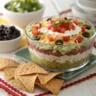 Seven layer dip in a glass dish with chips on the side