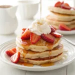 Strawberry pancakes topped with whipped cream and fresh strawberries