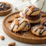 Almond Joy cookies topped with shredded coconut, almonds, and chocolate drizzle