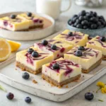 Lemon blueberry cheesecake bars with golden crust and fresh blueberries on a platter