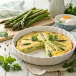 Golden asparagus frittata garnished with fresh herbs, served on a white plate.