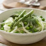 Fresh fennel salad with green peas, asparagus, and herbs in a bowl.