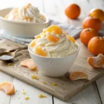 Flat lay of mandarin oranges, cake ingredients, whipped topping, and gelatin mix.