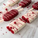 Red velvet cakesicles coated in white chocolate with crumbs and drizzle