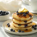 Stack of lemon blueberry pancakes with syrup, butter, and fresh berries