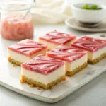 Layered no bake cheesecake squares topped with rhubarb compote on white plate