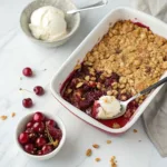 Warm cherry crisp with juicy baked cherries and a golden oat crumble topping in a ceramic baking dish.