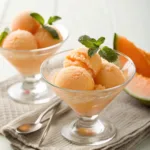Cantaloupe sorbet scoops in glass bowls with fresh melon garnish