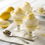 Lemon mousse in glass cups topped with whipped cream and lemon zest