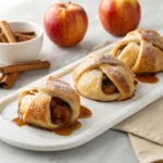 Homemade apple dumplings wrapped in flaky pastry with cinnamon syrup on a serving platter.