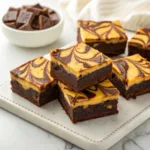 Homemade pumpkin cheesecake brownies with chocolate brownie layers and pumpkin cheesecake swirls on a serving platter.